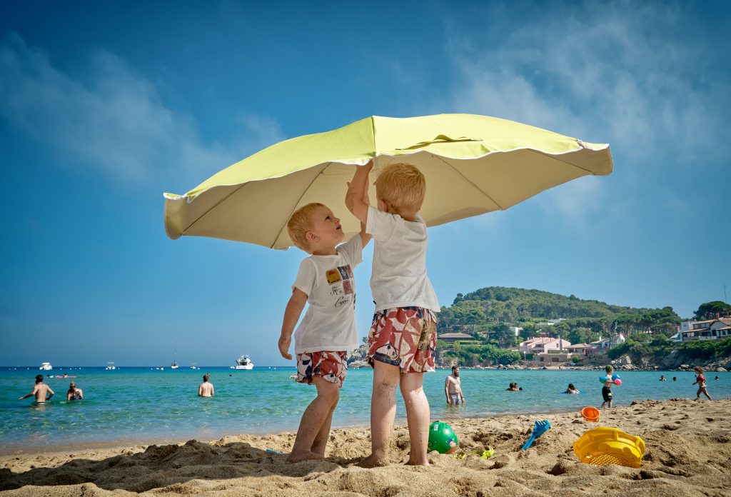 Das Bild zeigt Kinder am Strand unter einem Sonnenschirm.