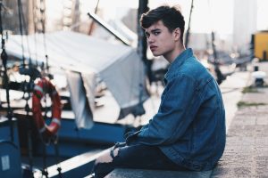 Das Bild zeigt einen jungen Mann an der Promenade sitzen.