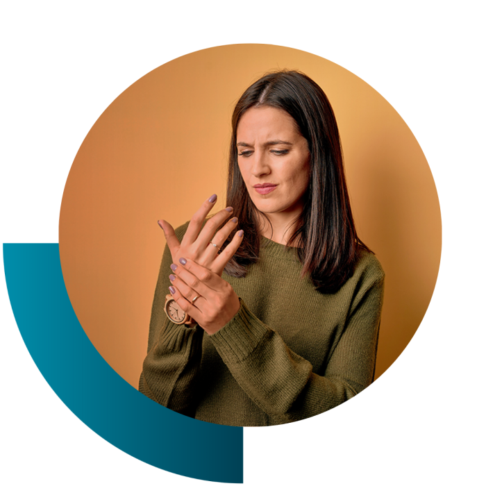 Das Bild zeigt eine Frau, die Schmerzen in ihren Händen hat, symptomspezifisch für Lupus.